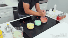 a man is mixing colored powders on a stove top with a measuring cup that says made in animatica