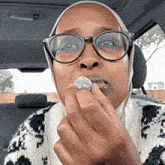 a woman wearing glasses and a hijab is biting a coin