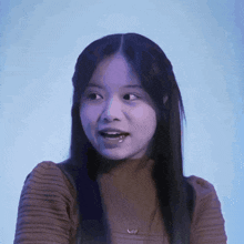 a girl with long hair is wearing a brown sweater and looking at the camera .