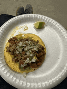 a taco on a paper plate with a lime wedge