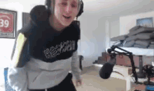 a man wearing headphones and a sweatshirt is standing in front of a microphone in a room .
