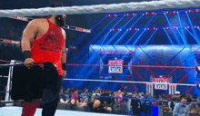 a wrestler in a red tank top stands in a wrestling ring