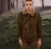 a man in a brown jacket is standing in front of a forest .