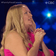 a woman in a pink dress is smiling with her hands folded in front of her face