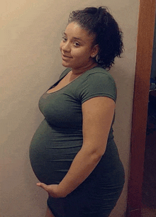 a pregnant woman in a green dress is holding her belly while standing in front of a door .