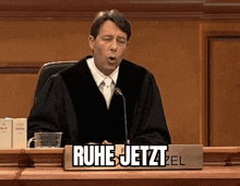 a man in a judge 's robe is sitting at a bench in a courtroom .