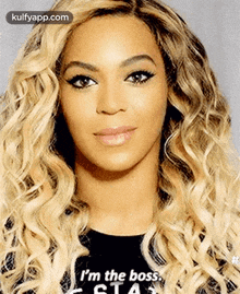 a close up of a woman with blonde curly hair wearing a black t-shirt that says i 'm the boss .
