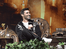 a man sitting in a chair holding a microphone and wearing a jacket that says facts