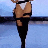 a woman in a white bikini and black boots is walking down a runway