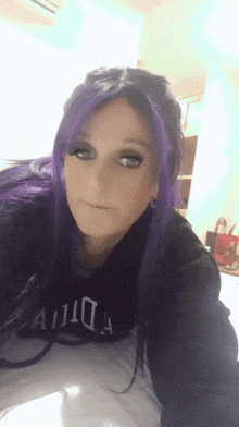 a woman with purple hair is wearing a black sweatshirt that says ' aida ' on it