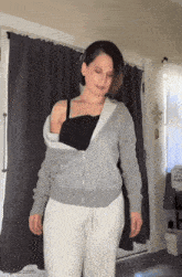 a woman is standing in front of a door wearing a grey hoodie and white sweatpants