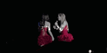 two women in red dresses are dancing on a stage while a man watches