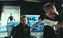 a woman is touching a man 's shoulder in front of a monitor