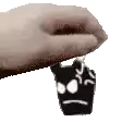 a hand is holding a black and white object with a face on it .