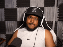 a man wearing headphones and a hat with the letter b on it is sitting in front of a microphone