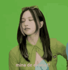 a woman in a green shirt is standing in front of a green screen and says mina de eliana .