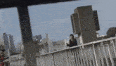 a man is standing on a bridge overlooking a city with a city in the background .
