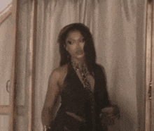 a woman in a black dress is standing in front of a white curtain holding a glass of wine .