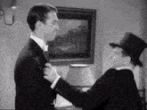 a man in a top hat is helping another man tie his tie .