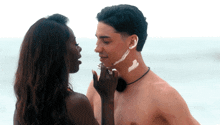 a woman applying sunscreen to a man 's face while they look into each other 's eyes
