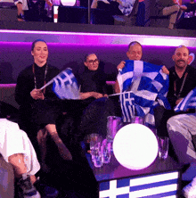 a group of people are sitting around a table holding flags one of which has the letter t on it