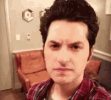 a man in a plaid shirt is making a funny face while taking a selfie in a living room .