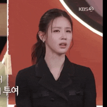 a woman in a black jacket with a ponytail looks at the camera with a kbs logo in the background
