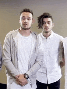 two men are standing next to each other in a room . one of the men is wearing a watch .
