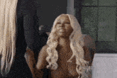 a naked woman with blonde hair is sitting in front of a mirror talking to another woman .