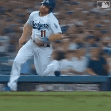 a baseball player wearing a dodgers jersey is jumping over a fence .