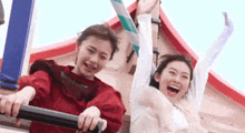 two young women are riding a roller coaster together and laughing