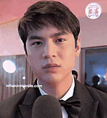 a man in a tuxedo talks into a microphone with wheninmanila.com written on the bottom right