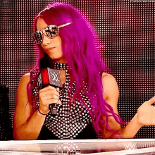 a woman with purple hair is holding a microphone in front of a crowd .