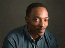 a man in a blue shirt is looking at the camera with a gray background .