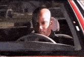 a bald man is driving a car and looking out the window