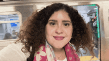a woman with curly hair and a scarf around her neck is smiling in front of a train