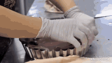 a person wearing gloves is putting a pie in a pan that says made in animatica on the bottom