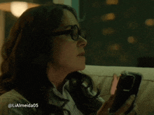 a woman sitting on a couch looking at a cell phone with the username lialmeida05