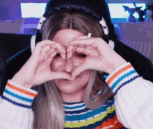 a woman wearing headphones making a heart with her hands