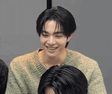 a young man wearing a green sweater is smiling while sitting next to another man .