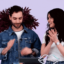 a man in a denim jacket and a woman in a white shirt applaud