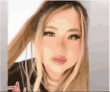 a close up of a woman 's face with long blonde hair and a necklace .
