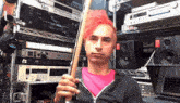 a man with pink hair is holding a drum stick in front of a rack of audio equipment