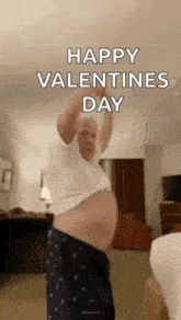 a man is dancing in a living room with his shirt off and a happy valentine 's day message .