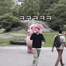 a man in a black sweater is walking in a park with a pink teddy bear in the background