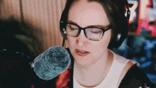 a woman wearing glasses and headphones is sitting in front of a microphone with her eyes closed .