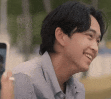 a young man is smiling while looking at a cell phone in a park .