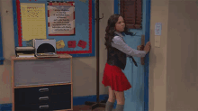 a girl in a red skirt is opening a blue door with the number 17a on it