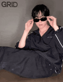 a man wearing sunglasses sits on the floor in front of grid