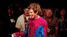 a man in a red and blue sweater is standing in front of a microphone